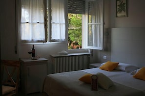 A bedroom with a bed, a bedside table with a bottle, and a window with curtains. - B&B Ortensia (Forte dei Marmi)