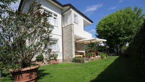 A two-story house with a stone pillar, a covered patio, and a well-maintained lawn. - B&B Ortensia (Forte dei Marmi)