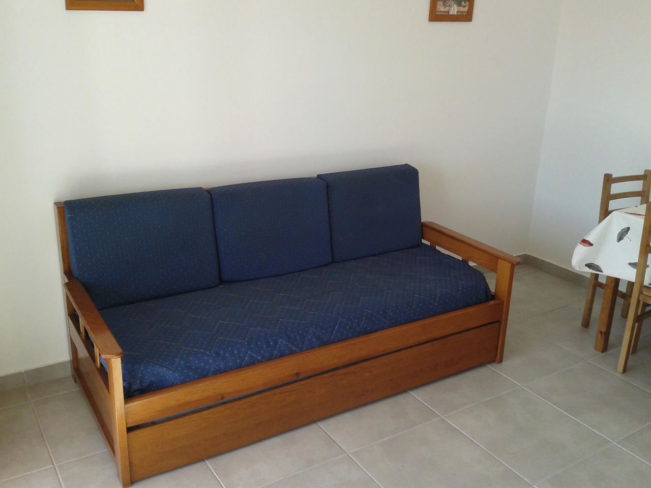 Um sofá de madeira com almofadas azuis em um quarto com piso de azulejos.