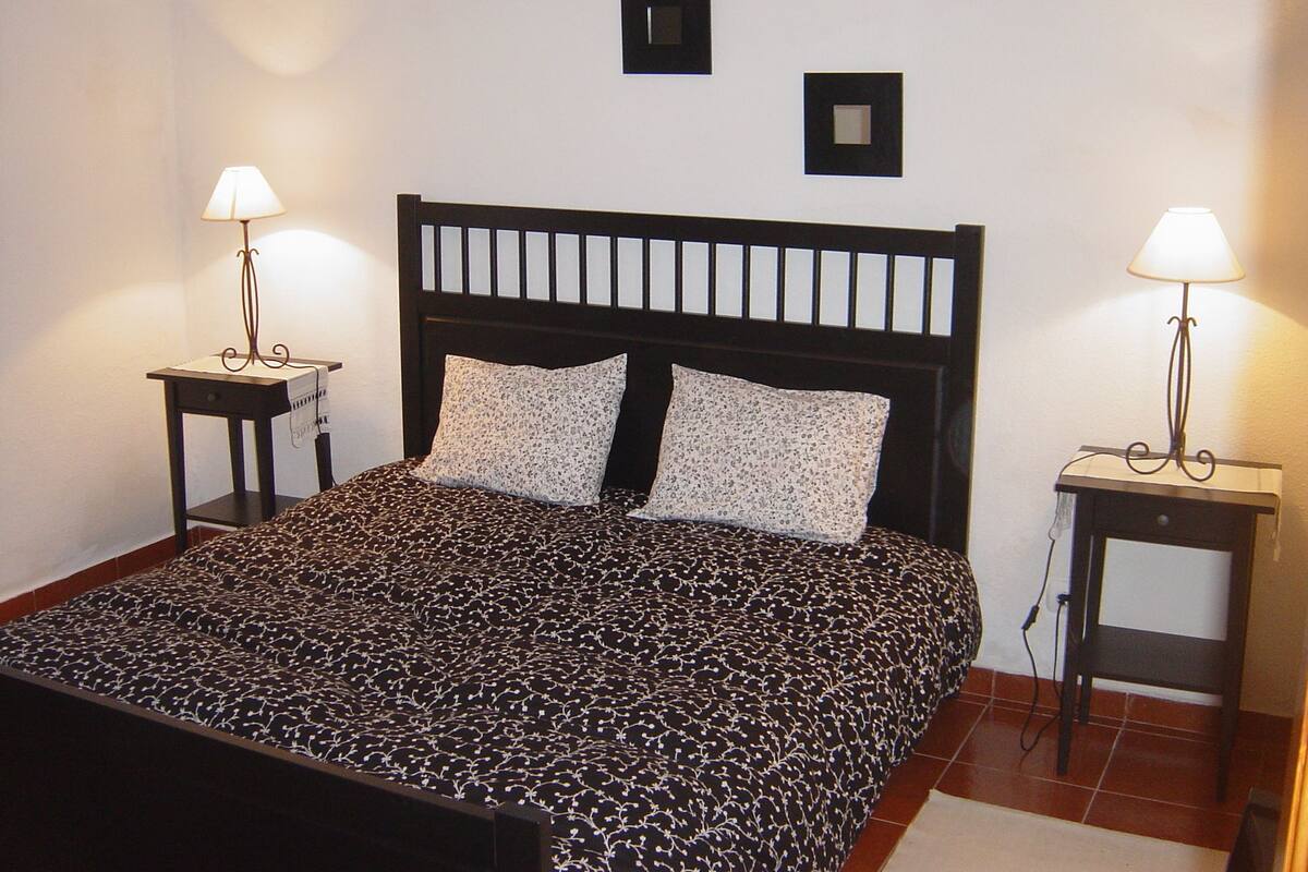 A neatly made bed with a patterned bedspread, two pillows, and two bedside tables with lamps.