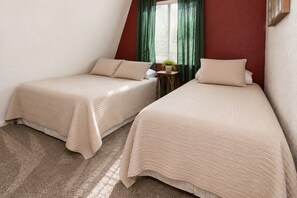Two single beds with beige bedding in a room with a red accent wall, a small table with a plant, and a window with green curtains. - Bear 'n Tree (Big Bear Lake)