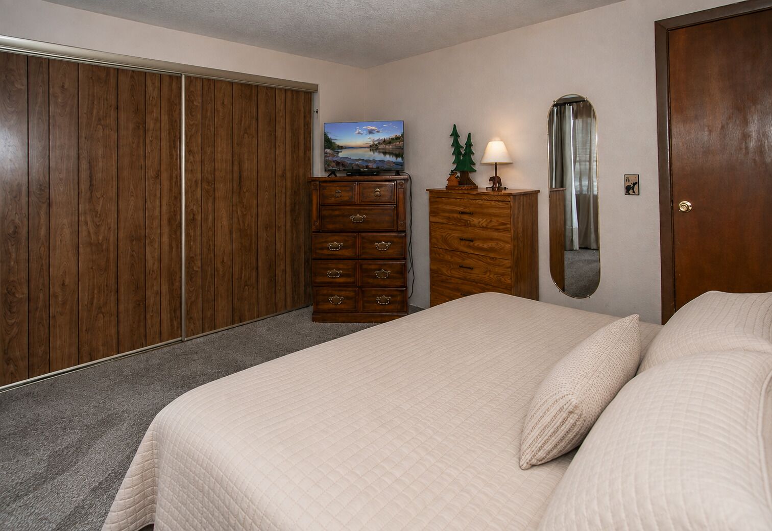 A bedroom with a bed, a dresser, a mirror, and a wardrobe.