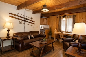A cozy living room with a leather sofa, wooden coffee table, and a dining area with a wooden table and chairs. - Bear 'n Tree (Big Bear Lake)