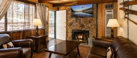 A cozy cabin interior with a stone fireplace, leather furniture, and a television mounted on the wall.