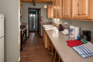A kitchen with wooden cabinets, a countertop, a stove, a sink, and a coffee maker. - Bear 'n Tree (Big Bear Lake)