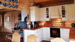 A cozy log cabin interior with a kitchen area featuring white cabinets, a stove, and a dining area with a wooden table and chairs. - Blazerbu - Cabin for 8 persons - Hol (Hol)