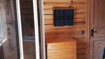 A wooden cabin with a shower enclosure, a wooden dresser, and a small sink.
