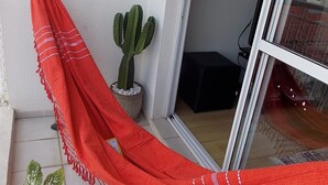A red hammock tied to a wall, a potted cactus, and a potted plant on a tiled floor. - Apartamento 2 dorms Metrô Saúde (São Paulo)