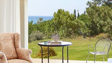 Un patio con una mesa redonda y sillas, con vista a un área verde con árboles y al mar.