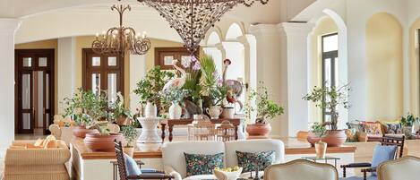 A spacious lobby with a grand chandelier, multiple seating areas, and a variety of potted plants.
