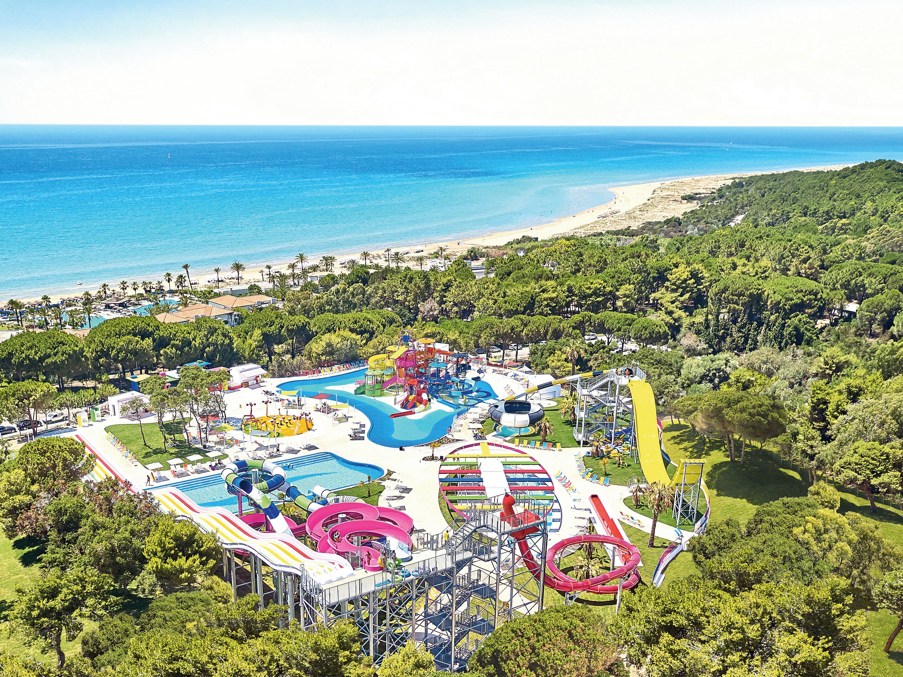 Ein Wasserpark mit mehreren Rutschen und Pools, umgeben von üppiger Vegetation und einem Strand.
