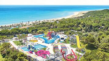 Ein Wasserpark mit mehreren Rutschen und Pools, umgeben von üppiger Vegetation und einem Strand.