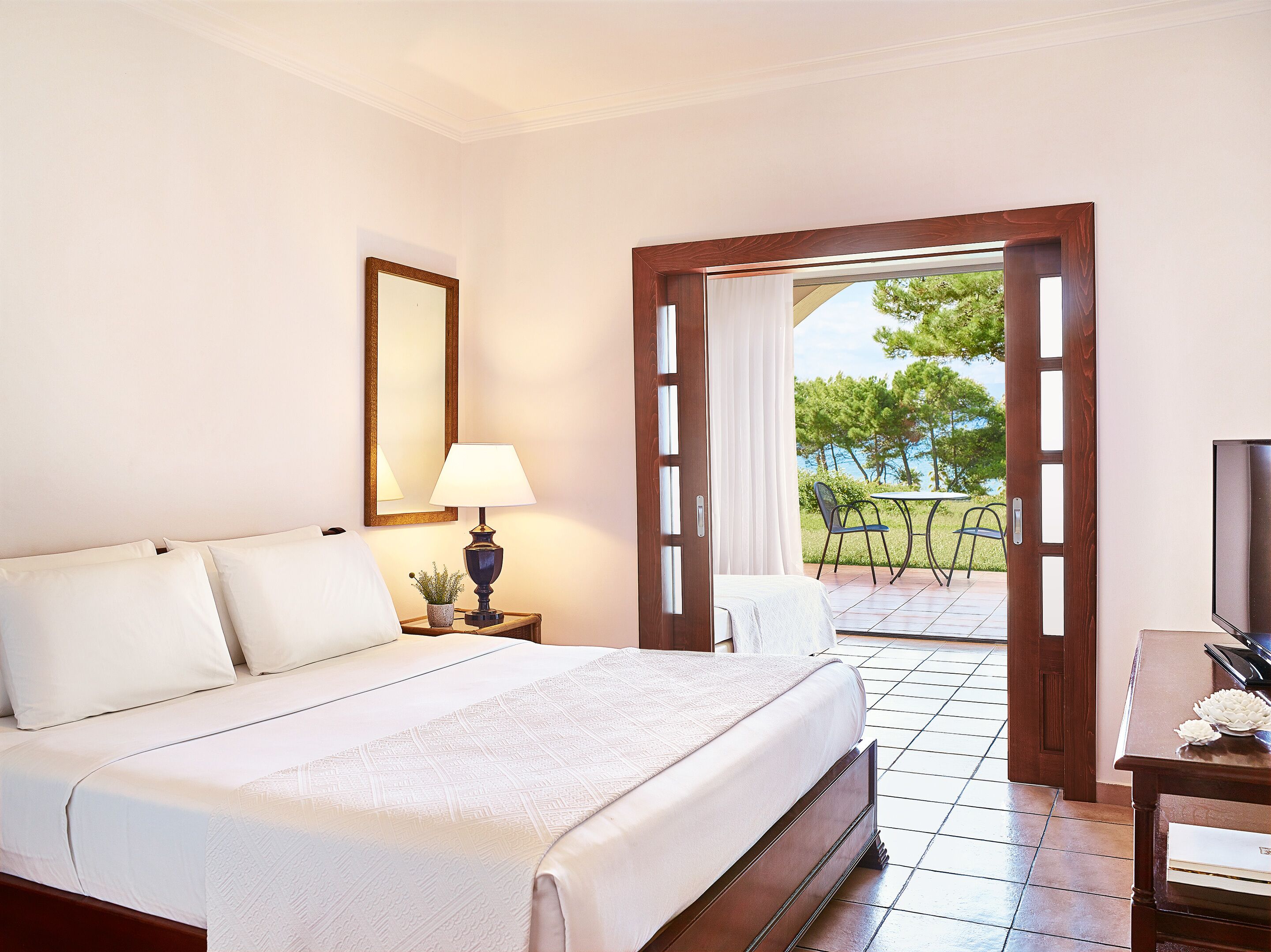 A hotel room with a bed, a lamp, a TV, and a view of the outdoors.