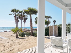 Une vue sur la plage, avec des palmiers, une terrasse en bois et des meubles d’extérieur blancs.
