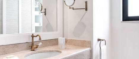 A bathroom with a marble sink, a brass faucet, a mirror, and a towel rack.