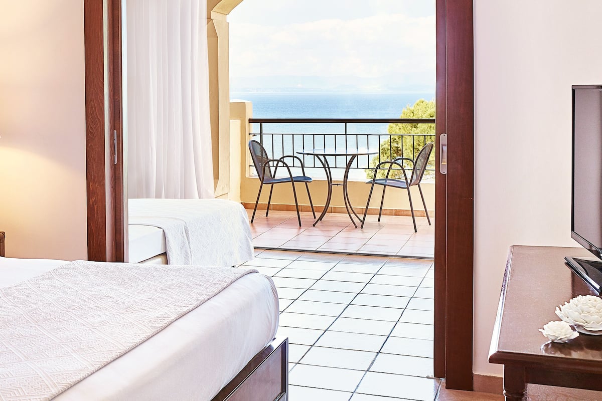 Habitación de hotel con una cama, una mesita y un balcón con vista al mar.