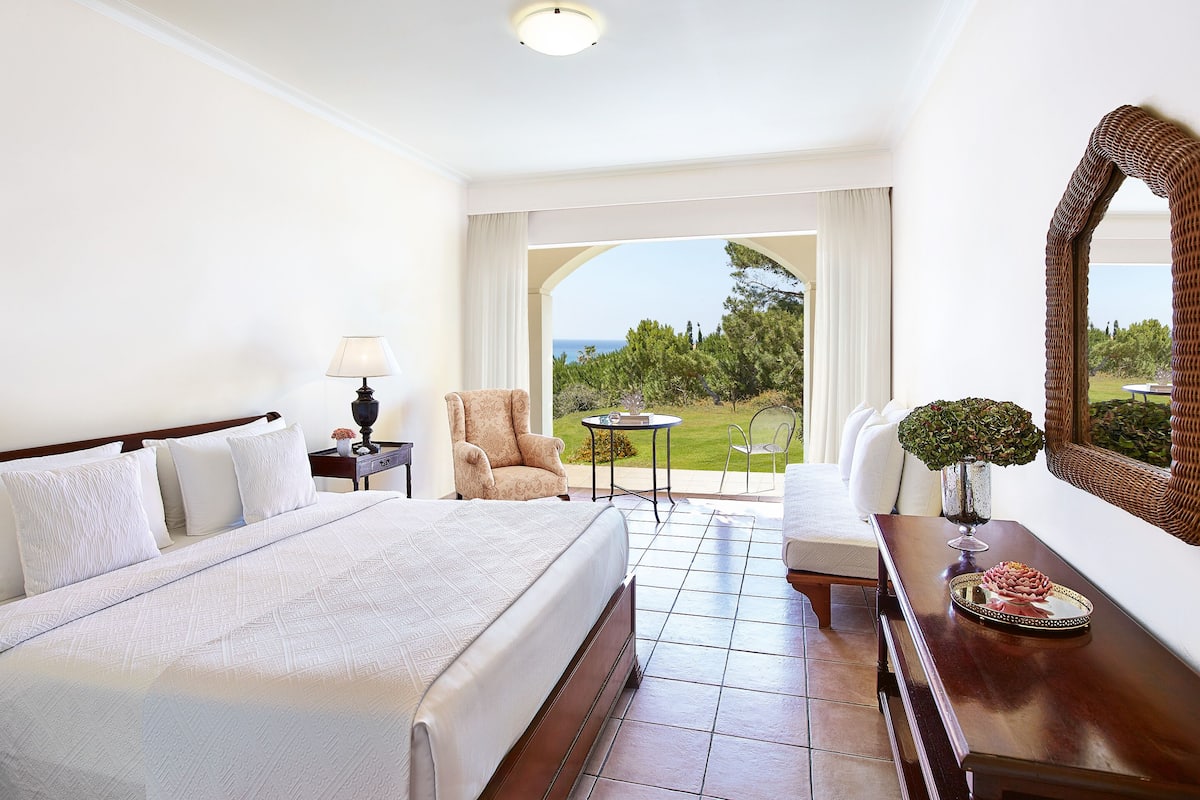 Habitación de hotel con una cama grande, un escritorio con lámpara, una silla y vistas al exterior.