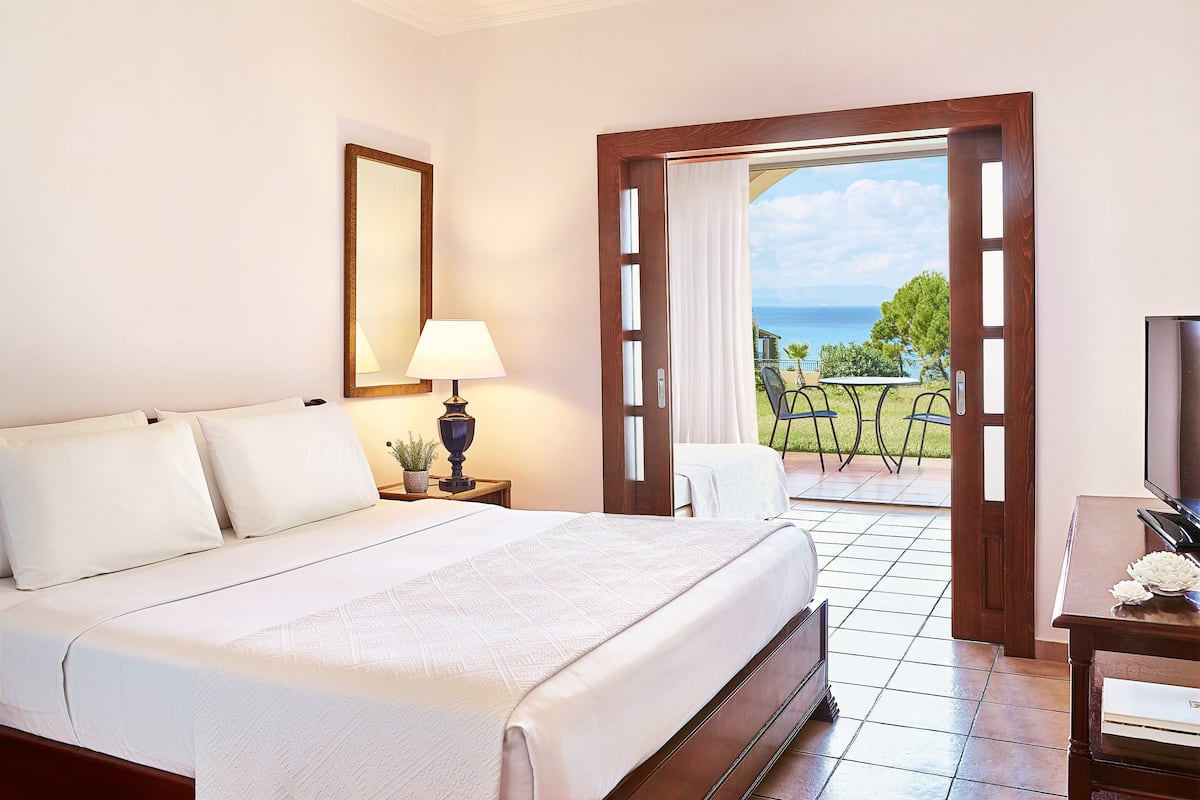Habitación de hotel con cama, mesita de noche con lámpara, televisor y vista al océano.
