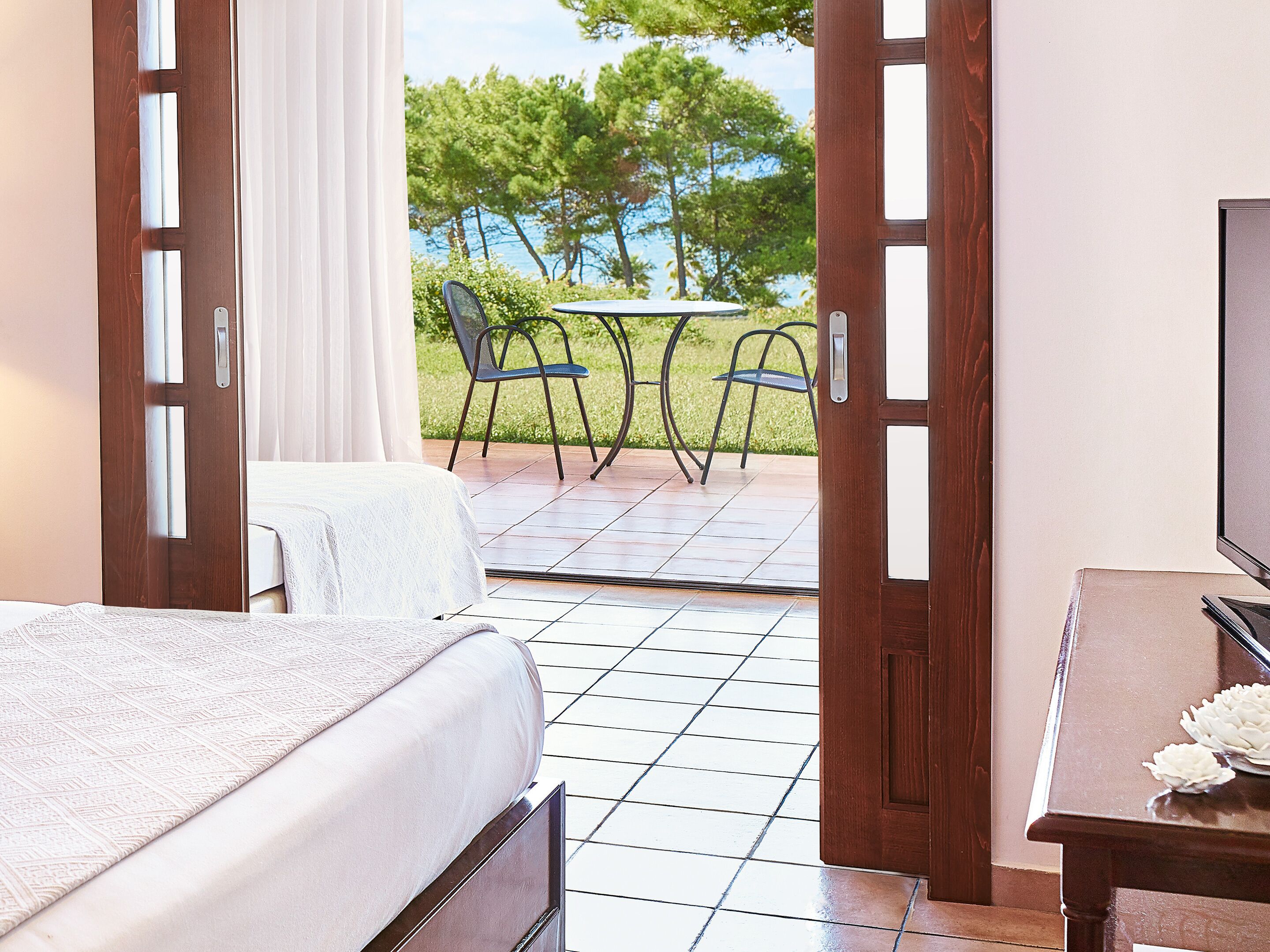 A hotel room with a bed, a TV, and a view of a patio with chairs and a table.