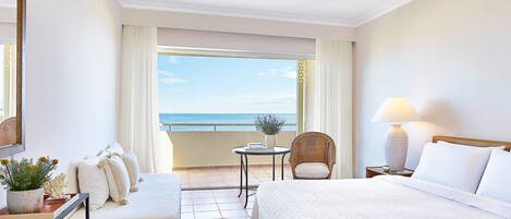 A hotel room with a bed, a chair, a small table, and a view of the sea.