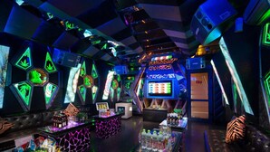 Zona de bar moderna con luces de neón, una pantalla grande mostrando gráficos coloridos y diverso equipo de bar.