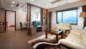 Una sala de estar moderna con televisor, asientos cómodos, una mesa de centro de vidrio y vista a la ciudad a través de amplias ventanas.