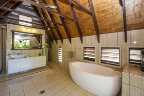 A modern bathroom with a freestanding bathtub, a large mirror, and a vanity with a sink. - Serene Place (Nelly Bay)