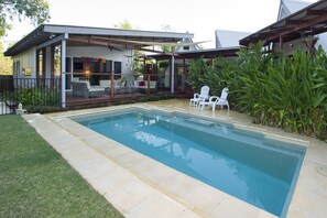 A swimming pool with a covered patio area, surrounded by greenery and a small deck with chairs. - Serene Place (Nelly Bay)