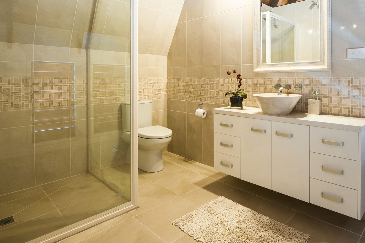A modern bathroom with a glass shower enclosure, a toilet, a sink with a vessel basin, and a mirror above the sink.