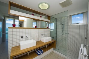 Ein modernes Badezimmer mit zwei Waschbecken, einer Duschkabine aus Glas und einem großen Spiegel über dem Waschtisch.