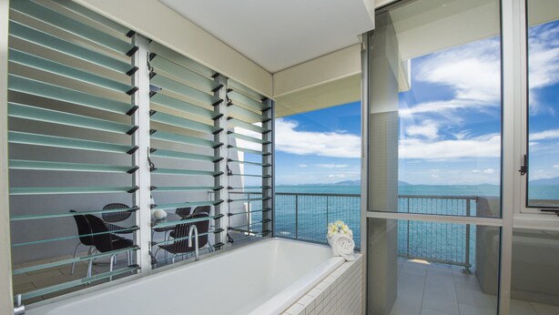 Een balkon met een glazen hekwerk, een wit bad en uitzicht op zee.