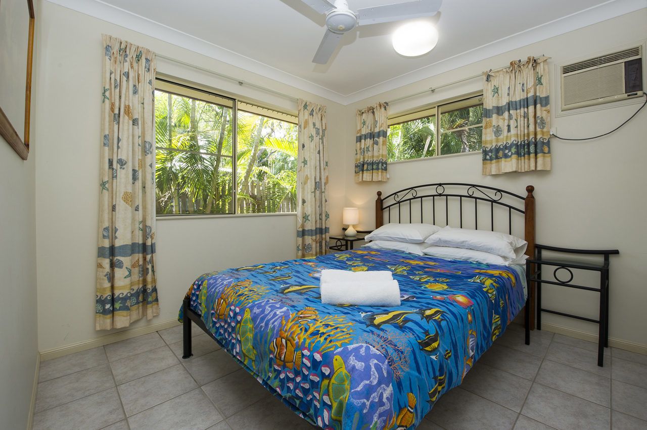 A bedroom with a bed, curtains, a ceiling fan, a window, and a nightstand with a lamp.