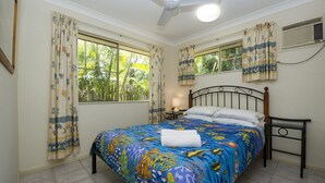 A bedroom with a bed, curtains, a ceiling fan, a window, and a nightstand with a lamp. - Island Dreams (Nelly Bay)