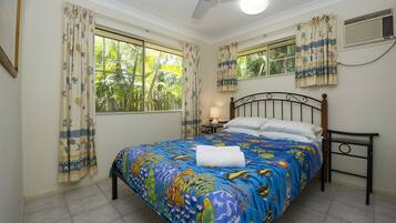 A bedroom with a bed, curtains, a ceiling fan, a window, and a nightstand with a lamp.