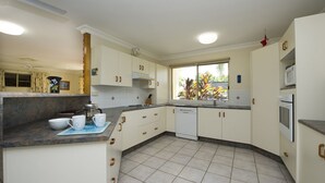 A kitchen with white cabinets, a dishwasher, a microwave, and a window with a view of plants. - Island Dreams (Nelly Bay)