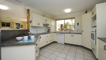 A kitchen with white cabinets, a dishwasher, a microwave, and a window with a view of plants.