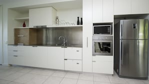 A modern kitchen with stainless steel appliances, white cabinetry, and a tiled floor.