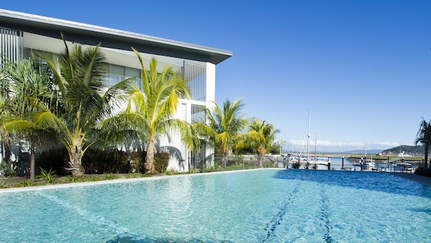 A modern hotel with a pool, palm trees, and a view of the marina.