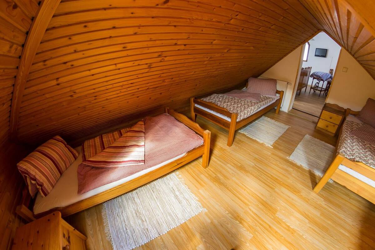 A cozy attic bedroom with two wooden beds, a small table, and a TV in the corner.