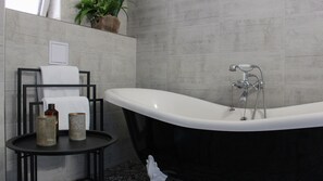 Un baño moderno con una bañera independiente, una mesita redonda pequeña con artículos de aseo y un perchero para toallas.