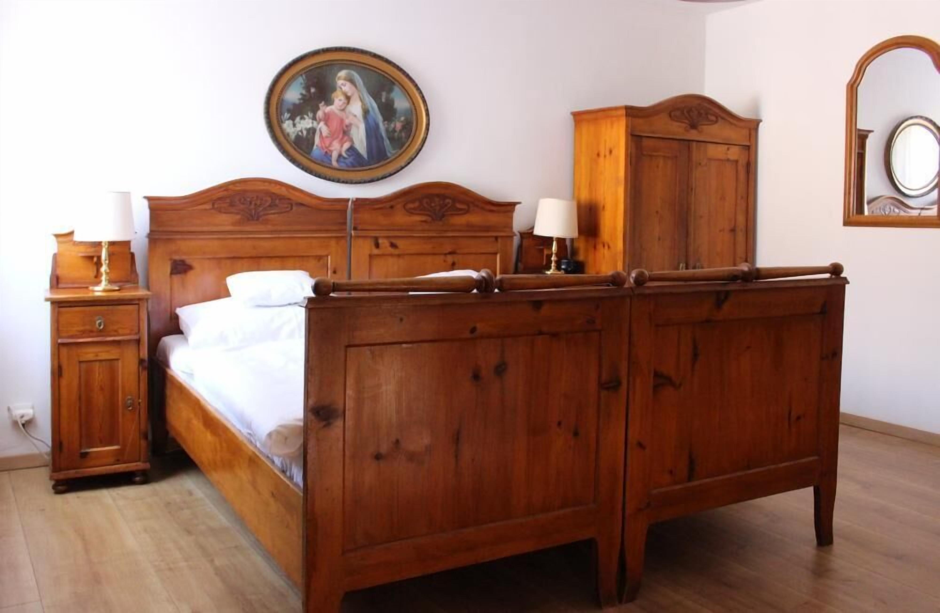 A wooden bed with a headboard, a nightstand, a dresser, a framed picture on the wall, and a mirror on the wall.