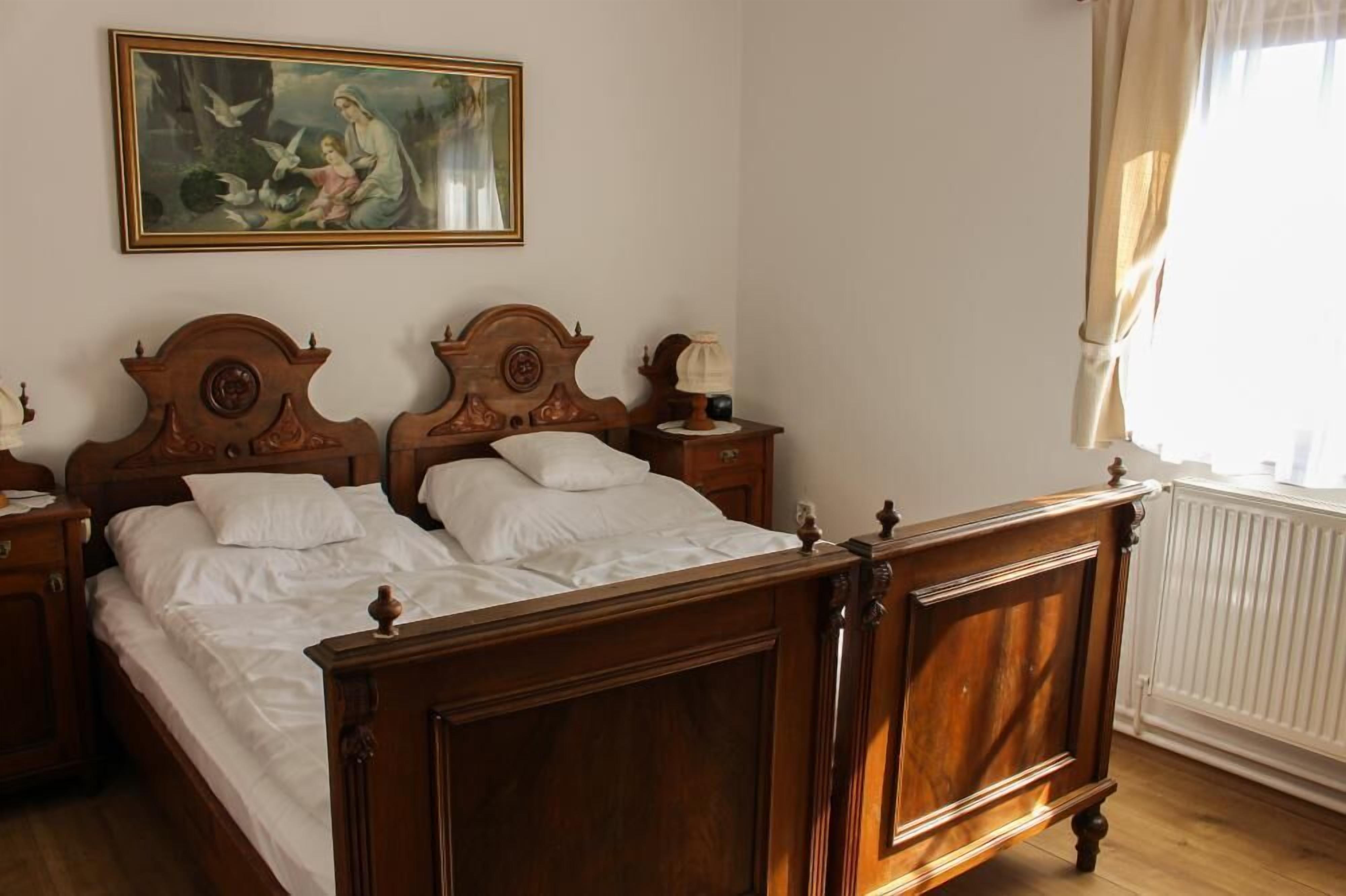 Un lit à baldaquin en bois, avec du linge de lit blanc, une table de chevet avec une lampe et un tableau au-dessus du lit.