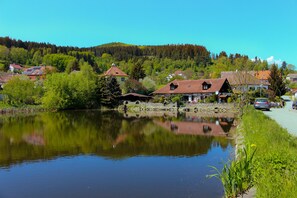 Un pueblo tranquilo junto al lago, con casas tradicionales, un lago sereno que refleja el paisaje, y un camino a lo largo de la orilla.