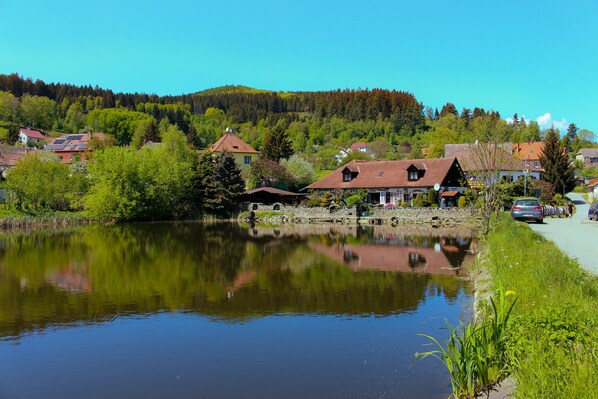 A serene lakeside village with traditional houses, a calm lake reflecting the scenery, and a pathway along the water's edge.