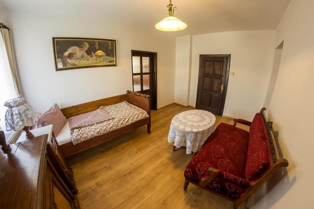 Una habitación pequeña y acogedora con una cama de madera, un sofá rojo, una mesita redonda y una puerta.