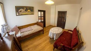 Una habitación pequeña y acogedora con una cama de madera, un sofá rojo, una mesita redonda y una puerta.