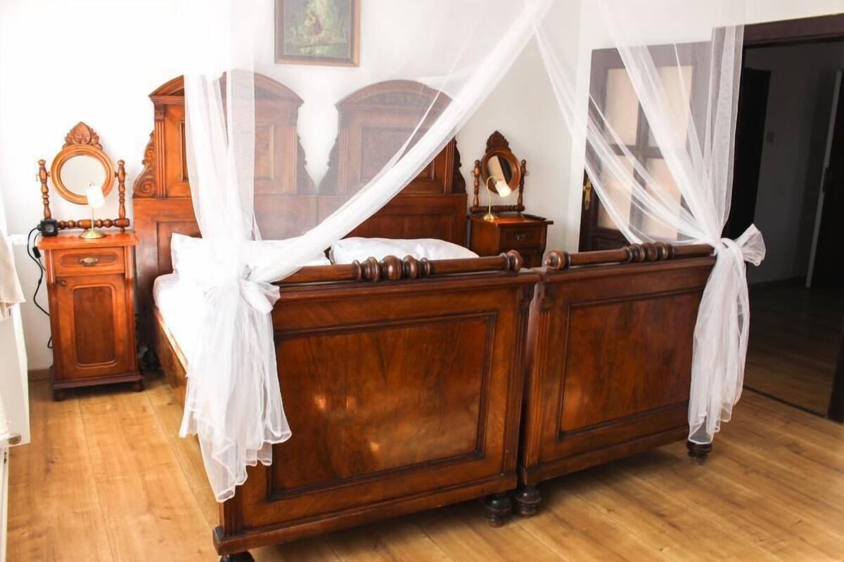 A wooden four-poster bed with a canopy, a wooden dresser, a mirror, and a bedside table with a lamp.