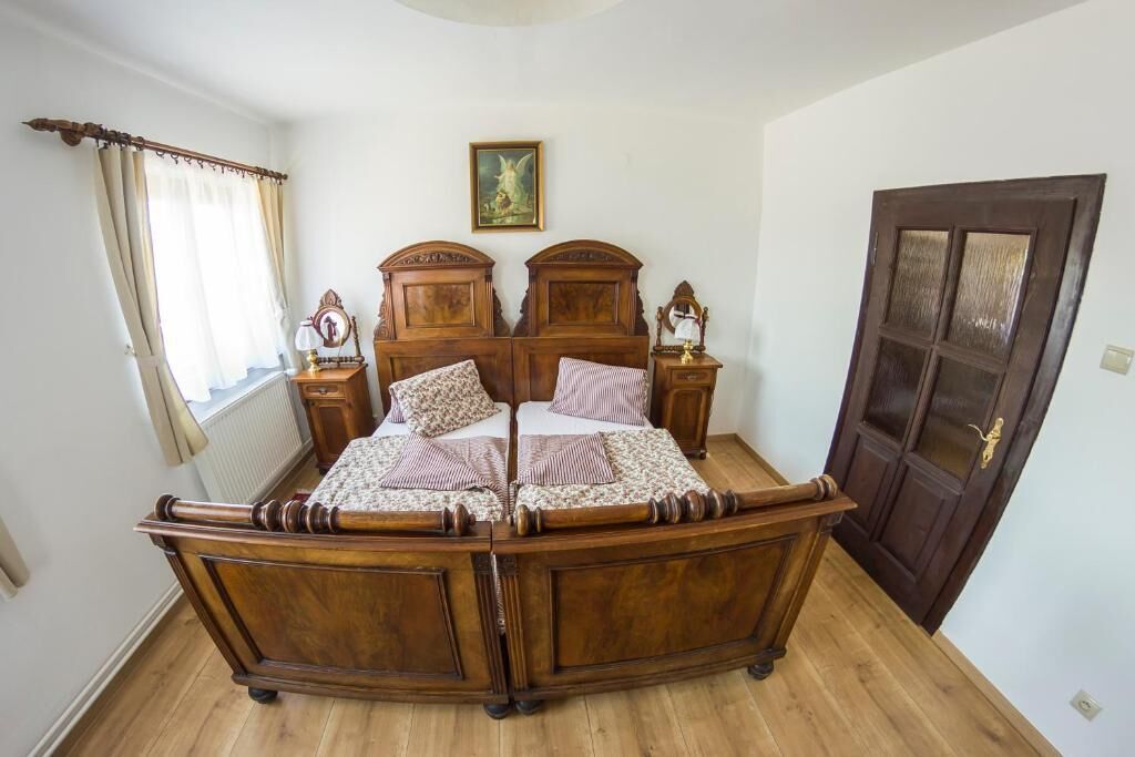 Een slaapkamer met een houten hemelbed, een nachtkastje met een lamp, een ingelijst schilderij aan de muur, en een deur met ruitpanelen.