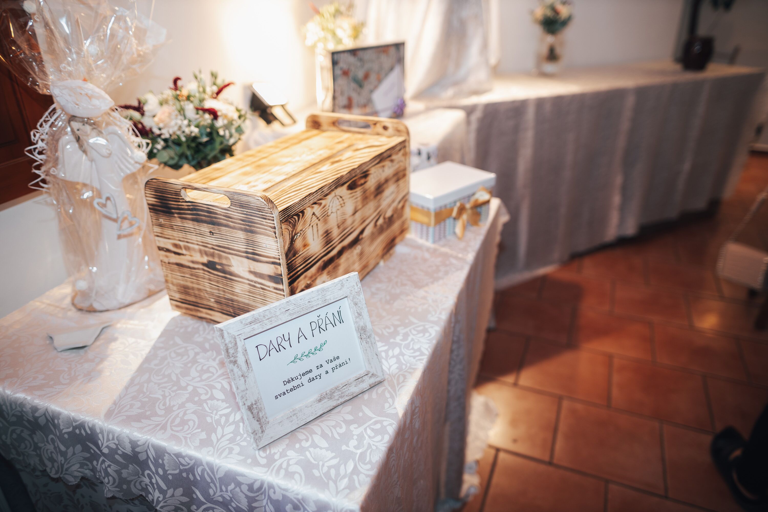 Ein Tisch mit weißer Tischdecke, einer Holzkiste und einem Schild mit der Aufschrift 'DARY A PRANĚ'.