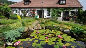 Una casa tradicional con techo de tejas, un jardín con un estanque y lirios acuáticos, y un pequeño puente.